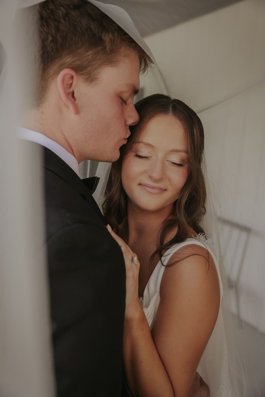 A groom leaning in to his bride against a white wall