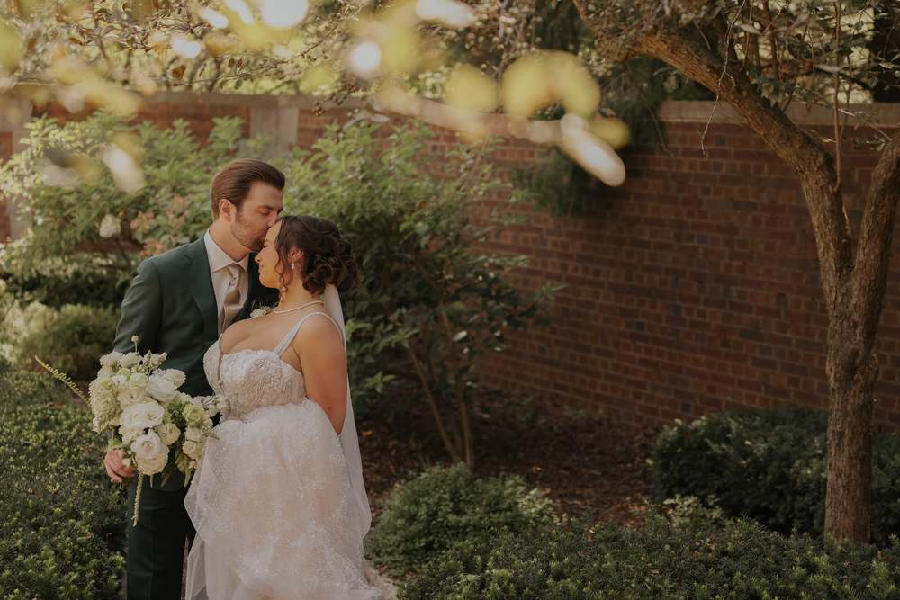 The couple beneath flowering branches by the brick wall